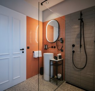 la-villetta_nido-zimmer-14-badezimmer.jpg Waschtisch mit rundem Spiegel, Fliesen in orange, weiße Tür, Dusche – Detail aus La Villetta, Zimmer 14